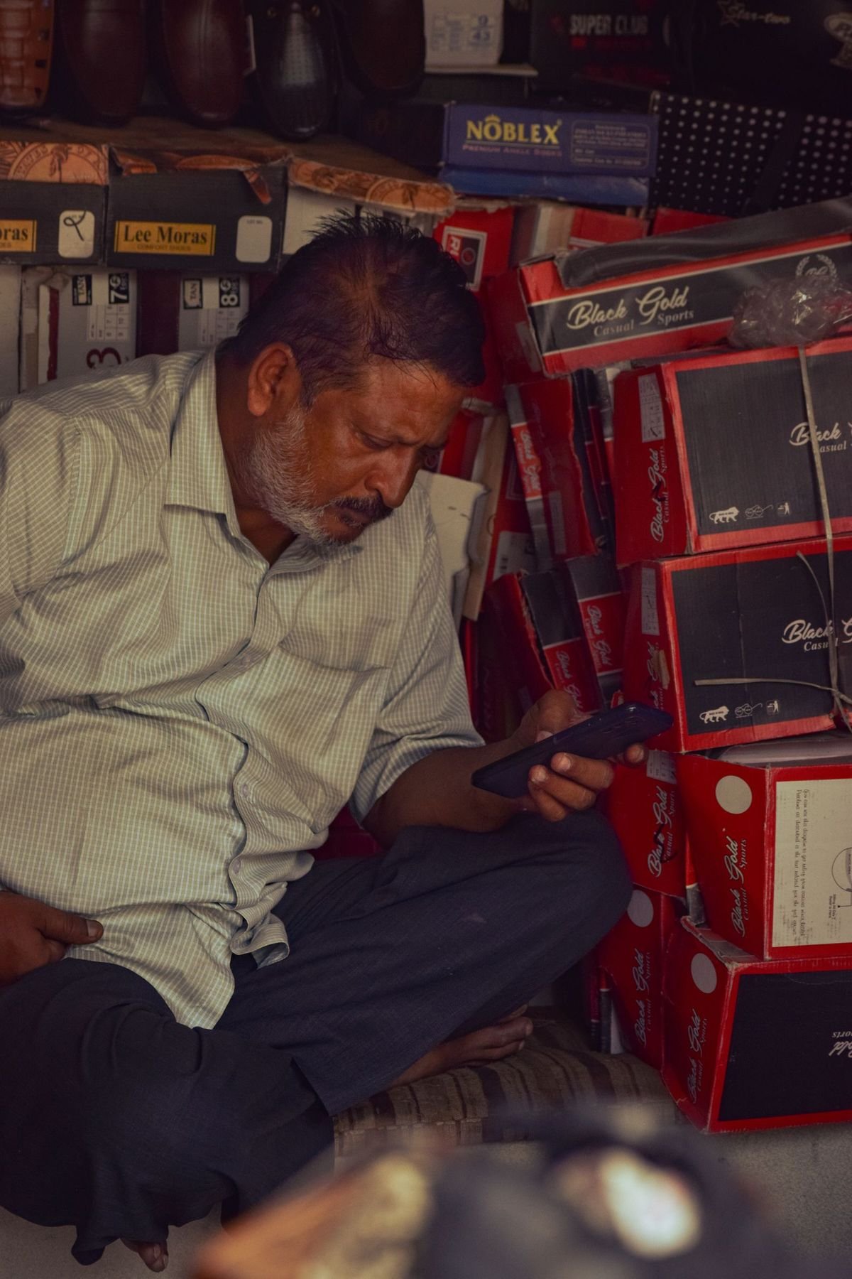 A shopkeeper checking messages on a phone inside a small shop