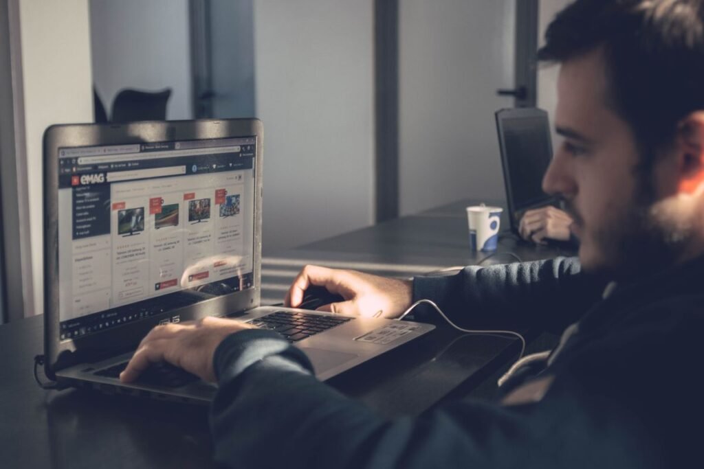 A man at a desk in an office using a laptop showing a website, with sunlight across the desk