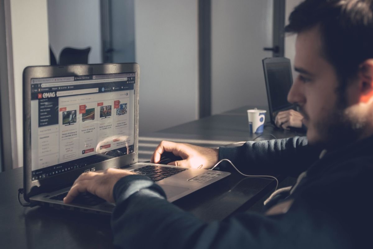 A man at a desk in an office using a laptop showing a website, with sunlight across the desk