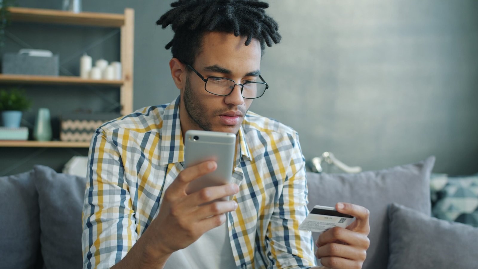 A customer holding a smartphone and a card while checking out online at home