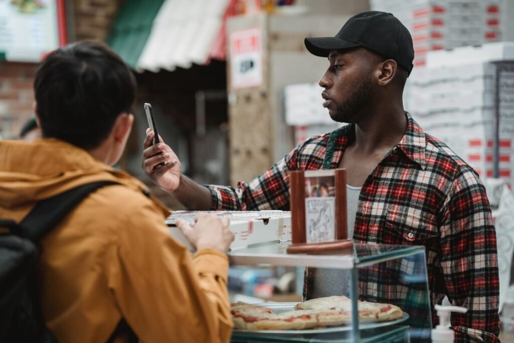 A shopkeeper holding a smartphone while talking with a customer at a shop counter