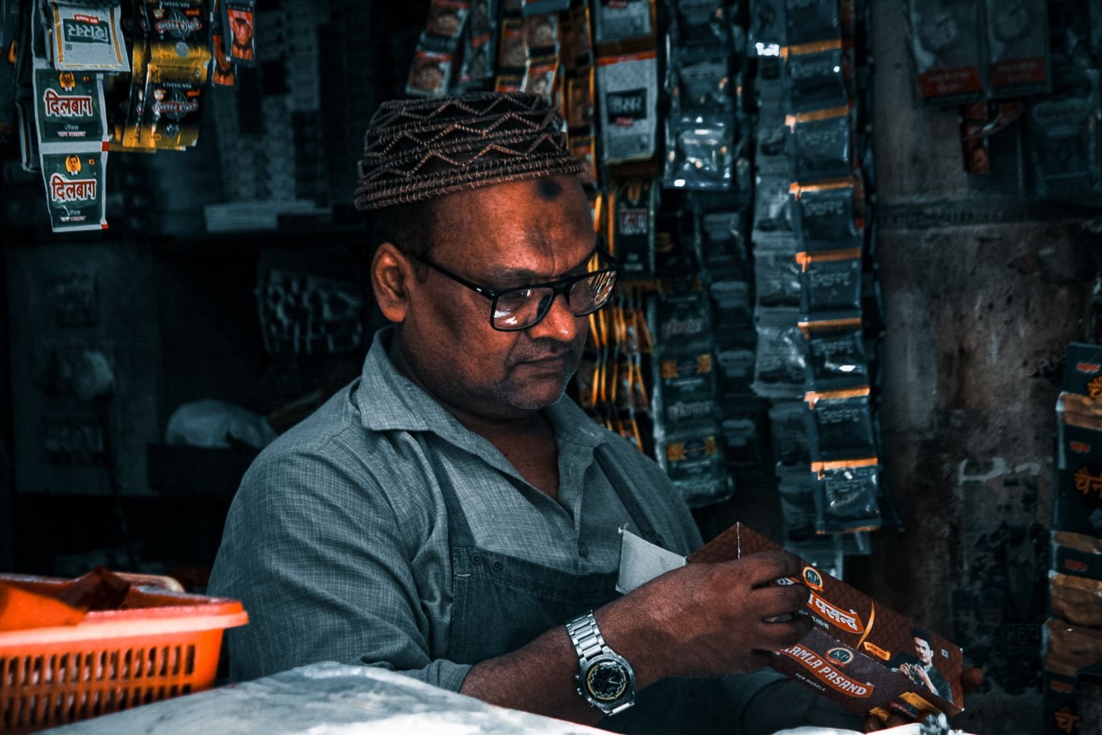 A South Asian shopkeeper arranges products on the shelves of his small store.